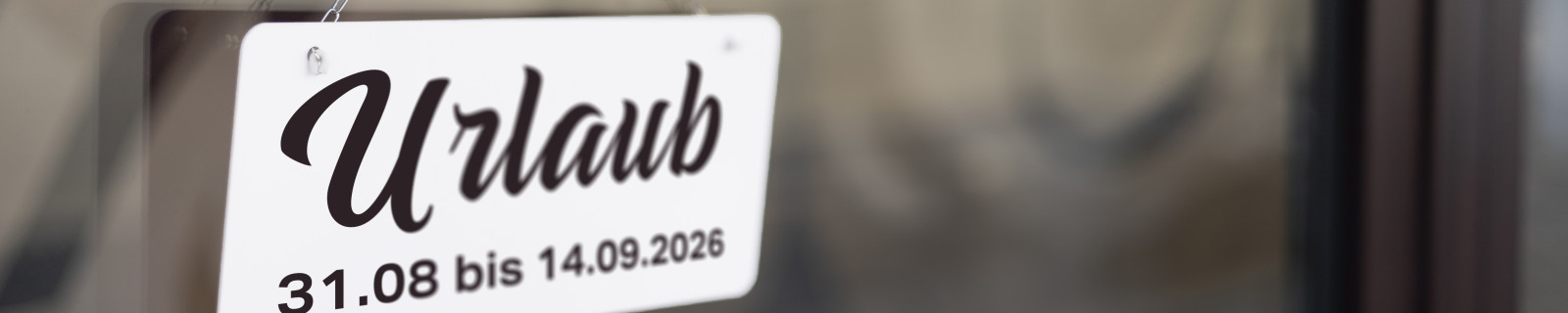 Schild mit Aufschrift 'Urlaub' und Datum 31.08 bis 14.09.2026 an einer Glastür.